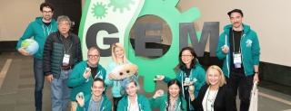 Members of the Human Practices' Committee standing and smiling in front of the iGEM Logo at the Giant Jamboree
